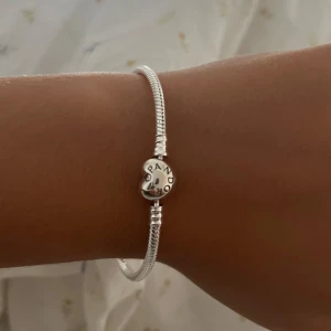 Silverarmband från Pandora - Säljer ett elegant silverarmband från Pandora. Armbandet har en klassisk design med en rund berlock som har Pandora-loggan ingraverad. Perfekt för både vardag och fest!