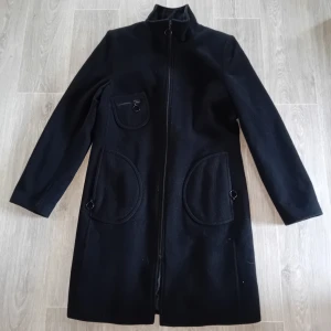 Svart ullkappa med dragkedja - Säljer en stilren svart kappa i ullblandning i storlek 38/40. Den har en dragkedja framtill och praktiska fickor.Perfekt för höst och vinter, och den är långärmad för extra värme. 