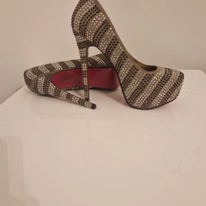 Glittriga pumps med hög klack - Säljer ett par superglittriga pumps med hög klack. De har en snygg randig design med massor av paljetter som verkligen fångar ljuset. Perfekta för en fest eller en utekväll när du vill sticka ut! Skorna har en spetsig tå och en elegant siluett.