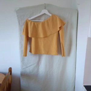 Gul offshoulder topp - Säljer en superfin gul offshoulder topp med volangdetaljer. Perfekt för en somrig look eller en festlig kväll. Toppen har långa ärmar och är i ett mjukt material som känns skönt mot huden.