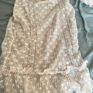 Blommig klänning från Karen Millen - Säljer en superfin blommig klänning från Karen Millen. Den har ett vackert mönster med små blommor i orange och grönt på en vit bakgrund. Klänningen är täckt med ett lager av vit spets som ger en romantisk känsla. Perfekt för sommarens fester eller en mysig vårdag!