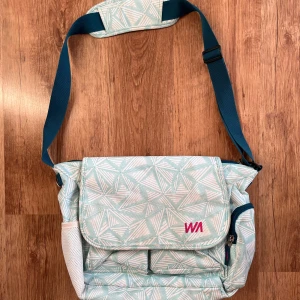 Mönstrad axelväska med justerbar rem - Säljer en superfin axelväska med ett unikt geometriskt mönster i ljusblått och vitt. Väskan har en justerbar axelrem i mörkblått och flera praktiska fack med dragkedjor. Perfekt för vardagsbruk eller när du är på språng. Den är i bra skick och redo för ett nytt hem!