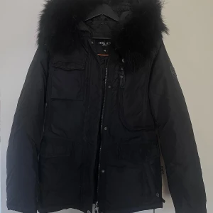 Svart vinterjacka från Hollies - Säljer en snygg och varm svart vinterjacka från Hollies i mycket bra skick. Jackan har äkta tvättbjörnspäls på huvan och flera praktiska och väldigt rymliga fickor inuti och utanpå med knappar och dragkedja. Perfekt för kalla vinterdagar! 🖤 ( Originalpris 4298kr ) 