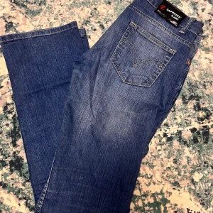 Blå jeans från Sapphire - Säljer ett par snygga blå jeans från Sapphire. De har en klassisk femficksdesign och en knappgylf. Jeansen är i en straight fit och har en lätt tvättad look som ger dem en cool, avslappnad stil. Perfekta för vardagsbruk!