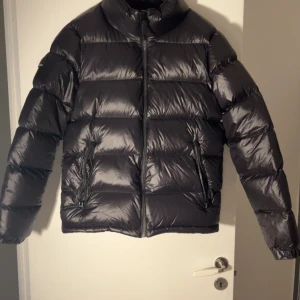 Svart pufferjacka från Superdry - Säljer en svart pufferjacka från Superdry. Den är perfekt för kalla dagar med sitt dunfoder som håller dig varm. Riktigt snygg. Den är i nyskick aldrig använd. 10/10. Nypris 1.200kr. Mitt pris 599.