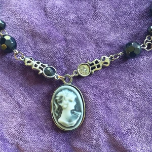 Svart pärlhalsband och örhängen med kamehänge - Säljer ett elegant set med ett svart pärlhalsband och matchande örhängen. Halsbandet har ett vackert kamehänge i svart och vitt, vilket ger en klassisk touch. En sten saknas se bild. 