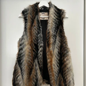 Väst i faux fur - Väst i väldigt fint skick, sparsamt använd. Den är från Newlook och är blandad med färgerna brun, svart, vit och beige. Mjuk och har två fickor.  Material: 65% modacrylic, 35% acrylic samt foder 100% polyester. 