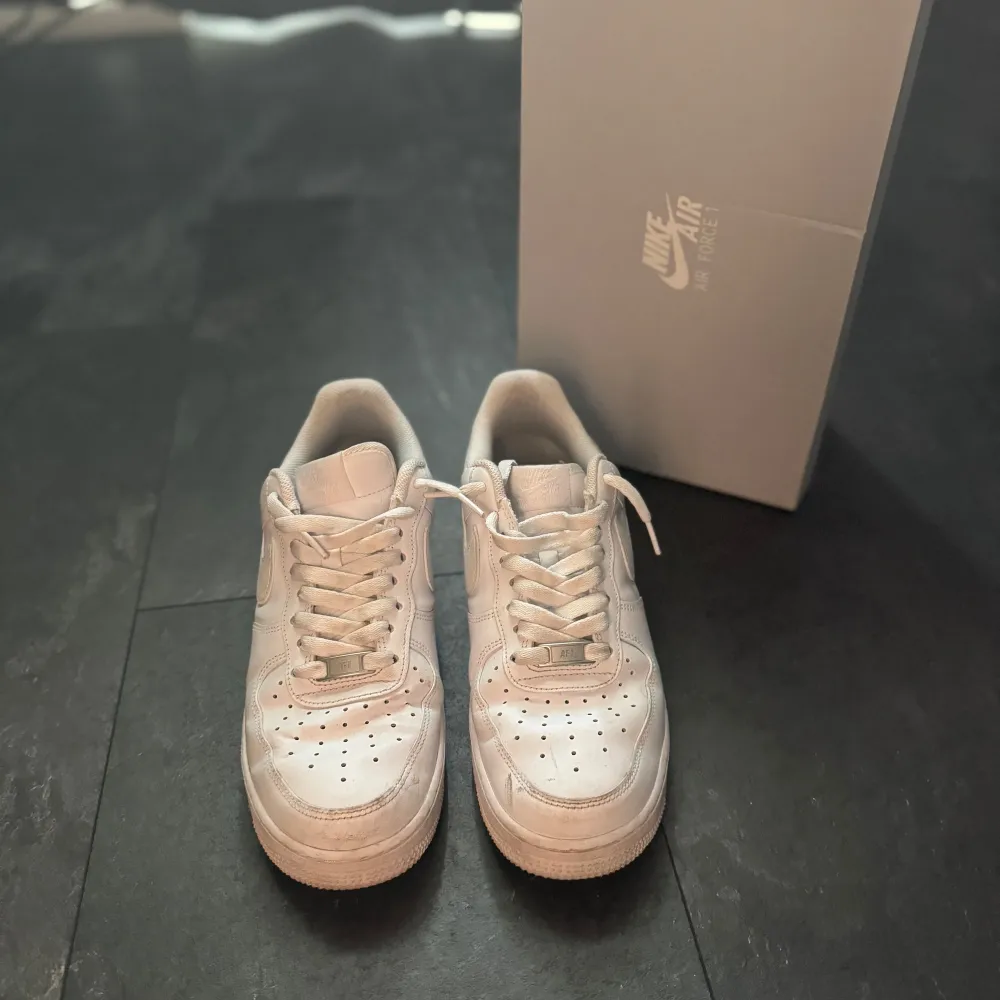 Säljer ett par klassiska vita Nike Air Force sneakers i 7/10. De har en stilren design med snörning och perforerade detaljer på ovansidan för extra ventilation. Perfekta för både vardag och fest!. Skor.