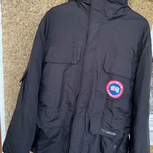 Säljer en svart vinterjacka från Canada Goose. Den är perfekt för kalla dagar med sin tjocka vaddering och långa ärmar. Jackan har en dragkedja framtill och flera praktiska fickor samt luva. Köptes på second hand. Perfekt för vintern.