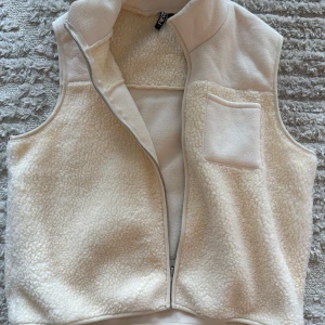 Vit fleeceväst från Pieces - Säljer en supermysig vit fleeceväst från Pieces. Den har en dragkedja framtill och en praktisk bröstficka. Perfekt för lager-på-lager under kyliga dagar. Västen är i bra skick