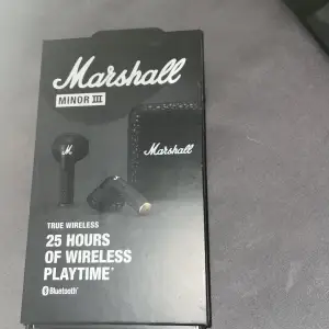 Säljer ett par Marshall Minor III True Wireless hörlurar. De är svarta och kommer med ett snyggt fodral med Marshall-loggan. Hörlurarna erbjuder 25 timmars trådlös speltid och ansluts via Bluetooth. Perfekt för musikälskare som vill ha stil och kvalitet i ett!