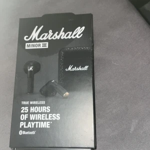 Marshall Minor III True Wireless Hörlurar - Säljer ett par Marshall Minor III True Wireless hörlurar. De är svarta och kommer med ett snyggt fodral med Marshall-loggan. Hörlurarna erbjuder 25 timmars trådlös speltid och ansluts via Bluetooth. Perfekt för musikälskare som vill ha stil och kvalitet i ett!