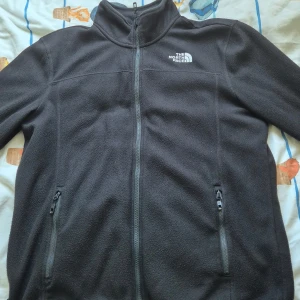 Svart fleecejacka från The North Face - Säljer en svart fleecejacka från The North Face i storlek L. Jackan har en dragkedja framtill och två praktiska fickor med dragkedjor. Perfekt för kyliga dagar och outdoor-äventyr. Den är i bra skick och redo för nya äventyr!