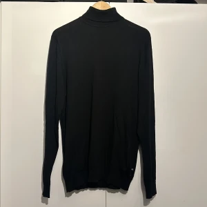 Svart polotröja från Matinique - Säljer en stilren svart polotröja från Matinique i storlek XL. Tröjan är tillverkad av 100% merinoull vilket gör den supermjuk och perfekt för kyligare dagar. Den har en klassisk passform med långa ärmar och en hög krage. Perfekt för både vardag och fest!