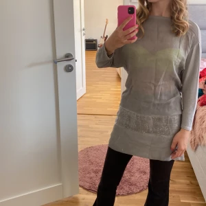Grå tunika med paljettdetaljer - Säljer en snygg grå tunika i storlek M. Den har trekvartsärmar och en glittrig paljettkant nedtill som ger en festlig touch. Perfekt för både vardag och fest!
