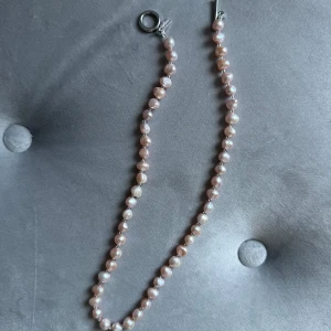 Pärlhalsband med rosa pärlor - Säljer ett elegant pärlhalsband med ljusrosa pärlor. Halsbandet har en stilren design med en silverfärgad låsdetalj. Perfekt för både vardag och festliga tillfällen! Äkta pärlor! 
