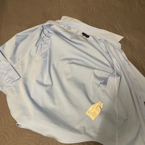 Ljusblå skjorta från Zara - Säljer en stilren ljusblå skjorta från Zara i storlek M. Skjortan har en klassisk design med knappar framtill och långa ärmar. Perfekt för både vardag och festliga tillfällen. Materialet känns mjukt och bekvämt mot huden.