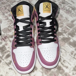 Nike Air Jordans i lila och gult - Säljer ett par Nike Air Jordans i superfräscht skick! De har en snygg kombination av lila, gult och vitt med svarta snören. Perfekta för att sticka ut i mängden. Skorna har en cool 'FAMILIA' detalj på sidan och den klassiska Air Jordan-loggan på tungan. Passar perfekt för både vardag och fest!