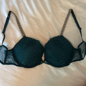 Mörkgrön bh från Victoria's Secret - Elegant mörkgrön bh med spetsdetaljer och justerbara axelband prydda med glittrande stenar. STORLEK 75C. Säljer pga fel storlek. Aldrig använt 