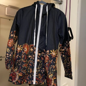 Blommig tröja med huva - Säljer en superfin tröja med blommigt mönster i rött, orange och gult. Tröjan har en praktisk huva och dragkedja framtill. Perfekt för kalla  dagar och ger en färgglad touch till din outfit! 🌧️🌸helt ny