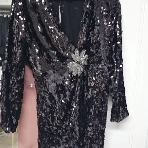 Svart glittrig klänning med paljetter - Snygg svart klänning täckt av glittriga paljetter med en v-ringad design. Klänningen har trekvartsärmar och en vacker broderad detalj i midjan som ger en extra touch av elegans. 