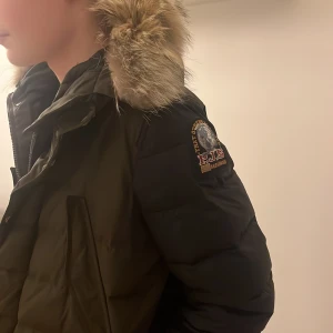 Svart dunjacka med päls  från Parajumpers - Snygg svart dunjacka från Parajumpers med päls på huvan. Jackan har praktiska fickor framtill. Perfekt för kalla dagar med sin varma och vadderade design. Använd nästan ingenting, köpt för 14 000