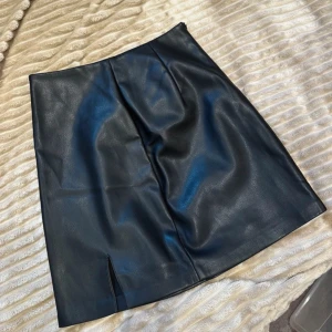 Svart kjol från Amisu - Snygg svart kortkjol från Amisu i skinnimitation. Kjolen har en liten slits i fram. Helt ny med prislapp