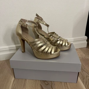 Guldiga klackskor med remmar - Eleganta guldiga klackskor med remmar och justerbart spänne runt ankeln. Skorna är använda men i bra skick