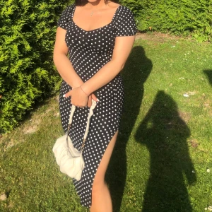 Svart prickig klänning - Snygg svart klänning med vita prickar och korta ärmar. Den har en slits på sidan och en v-ringad hals. Perfekt för soliga dagar! St 36-38