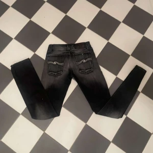 Svarta jeans från Nudie Jeans - Snygga svarta jeans från Nudie Jeans med en tight passform. De har en klassisk femficksdesign och en diskret tvätt för en cool look. Perfekta för en stilren outfit. Strl w26 l32. Pris kan absolut diskuteras 