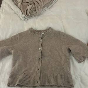 Beige kofta från & Other Stories - Säljer en stilren beige kofta från & Other Stories. Koftan har korta ärmar och knappar framtill, perfekt för lager-på-lager. Den är tillverkad i ett mjukt material som ger en lyxig känsla.