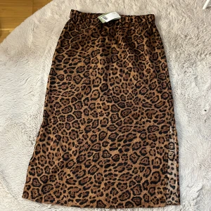 Leopardmönstrad kjol - Säljer en supercool leopardmönstrad kjol i brunt och svart. Kjolen är i ett mjukt och glansigt material, perfekt för att sticka ut på festen eller bara för en vardagslook med attityd. Den har en elastisk midja för extra komfort. Passar perfekt till både sneakers och klackar! Men slits på båda sidorna.