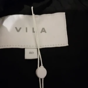 Svart vadderad kappa från Vila - Säljer en svart vadderad kappa från Vila i storlek 40. Perfekt för kalla dagar med sin långa design och knappar framtill. Håller dig varm och stilren hela vintern! 🖤