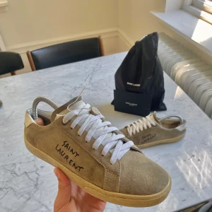 Saint Laurent sneaker  - Snygga beige sneakers från Saint Laurent med vit snörning och handskriven logga på sidan. Skorna är i väldigt bra skick och är i storleken 40 men passar också 41. Skorna är köpta och har kvitto på saint laurent så är såklart äkta och har blivit äktighetskollade av vestiare clothing. Pris kan dirksuteras vid snabb affär!