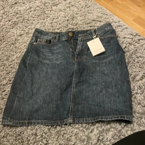 Jeanskjol från Samsøe Samsøe - Snygg jeanskjol från Samsøe Samsøe i klassisk blå denim. Kjolen har en knapp och dragkedja framtill samt två bakfickor. Perfekt för en avslappnad stil.