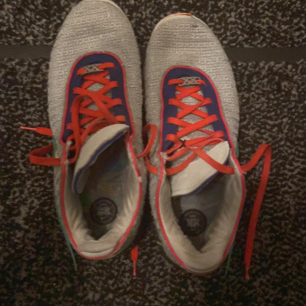 Snygga Nike sneakers med en unik färgkombination av grått, blått och orange. Skorna har röda snören och en mönstrad sula i blått och rosa. Perfekta för den som vill sticka ut med sin stil.. Skor.