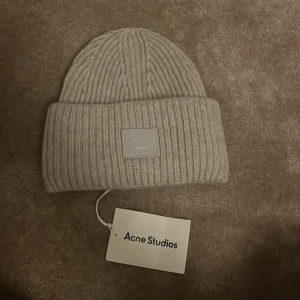 Grå acne mössa - Snygg grå stickad mössa från Acne Studios med ribbad design och ett stilrent märke framtill. Helt ny aldrig använd säljer för fel present. Lapp fins kvar