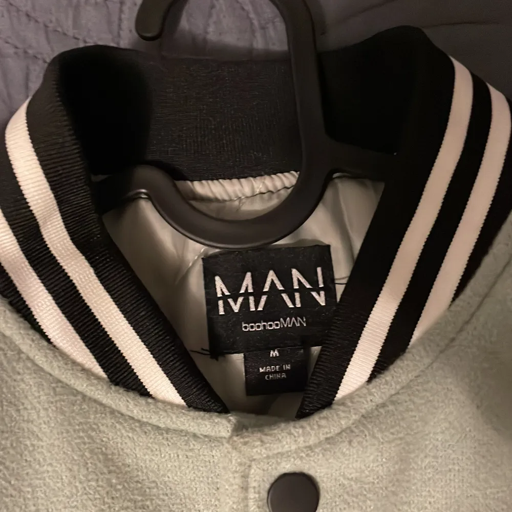 Snygg grön och vit bomberjacka från boohooMAN med broderade detaljer och stora bokstäver. Jackan har knappar framtill och randiga muddar vid krage, ärmslut och nederkant. Perfekt för en cool och avslappnad stil.. Takit.
