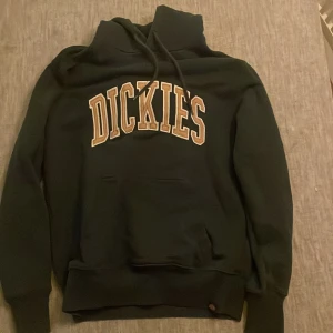 Svart hoodie från Dickies - Säljer en svart hoodie från Dickies i storlek S. Den har en stor broderad logga på bröstet och en klassisk ficka framtill. Perfekt för höst och vinter, med en skön passform och justerbar huva. Grym för både chill och vardagsäventyr!