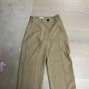 Snygga beige kostymbyxor från Bershka i storlek 38. De är högmidjade med en klassisk rak passform och har en stilren design med knappdetalj. 