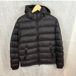 Svart dunjacka från Massimo Dutti - Säljer en snygg svart dunjacka från Massimo Dutti. Den är perfekt för vintern med sin quiltade design och dragkedja framtill. Jackan har en huva och två praktiska fickor med dragkedja. Den är i mycket bra skick och passar perfekt för kalla dagar. Perfekt för dig som vill hålla stilen i vinter! Modellen är 185 och sitter perfekt på han!