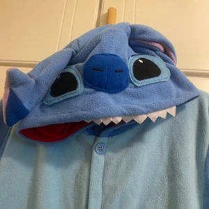 Stitch dräkt  - En stitch dräkt i storlek S, fickor på sidan. Dräkten har även en liten boll som svans på baksidan. Är i nyskick och använd en gång. Perfekta presenten till ett litet barn. 150 cm lång.