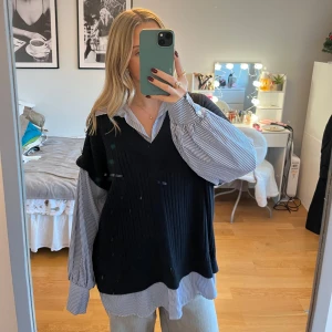 Svart stickad väst från River Island - Snygg svart stickad väst från River Island, perfekt för lager-på-lager-stil. Den har en ribbad struktur och är kombinerad med en randig skjorta under för en trendig look. Passar utmärkt till både vardag och mer uppklädda tillfällen.