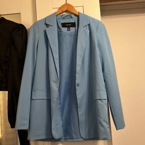 Ljusblå kavaj från Vero Moda - Säljer en stilren ljusblå kavaj från Vero Moda i storlek 34. Perfekt för både vardag och fest! Kavajen har en klassisk design med en knapp framtill och långa ärmar. Den är tillverkad i ett mjukt och bekvämt material som ger en snygg passform.