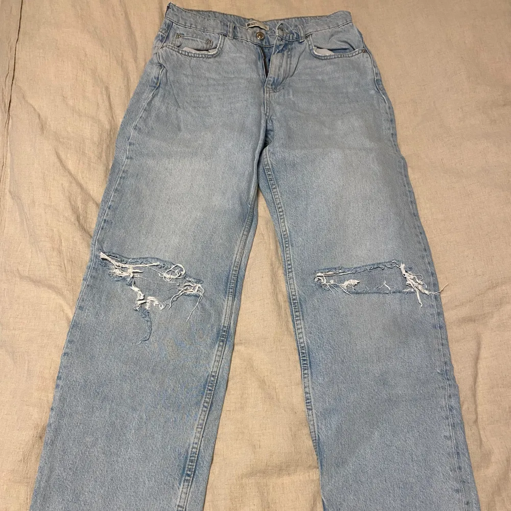 Säljer ett par ljusa jeans från Gina Tricot i storlek 38. De har en cool, sliten look med revor på båda benen. Perfekta för en avslappnad stil! Passar bra till sneakers eller boots.. Jeans & Byxor.