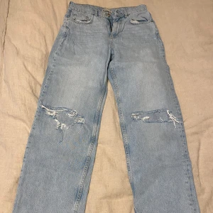 Ljusa jeans med slitningar från Gina Tricot - Säljer ett par ljusa jeans från Gina Tricot i storlek 38. De har en cool, sliten look med revor på båda benen. Perfekta för en avslappnad stil! Passar bra till sneakers eller boots.
