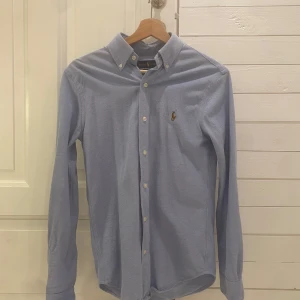 Blå skjorta från Ralph Lauren - Säljer en snygg blå långärmad skjorta från Ralph Lauren i storlek XS. Skjortan är i oxfordstil med klassiska knappar och en broderad logga på bröstet. Perfekt för både vardag och fest! 💙