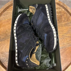 Stilrena valentino rockrunners - Säljer ett par äkta snygga Limited edition valentino rockrunners i ett mycket bra skick. De har ett coolt  och unikt blått camouflage-mönster med nitar runt sulan. Perfekta för att ge din outfit en unik touch! Skorna är i storlek 40 men passar 41. Även 42 kan funka vid normalt breda fötter. originalförpackning med dustbag, valentinokort och valentinosnören tillkommer!