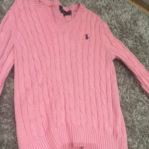 Rosa stickad tröja från Polo Ralph Lauren - Säljer en superfin rosa stickad tröja från Polo Ralph Lauren. Den har en klassisk kabelstickad design och en snygg v-ringning. Perfekt för både höst och vår! Tröjan är i mycket bra skick och har långa ärmar. Passar perfekt för en stilren och bekväm look.