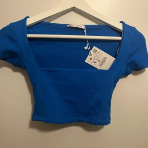 Blå croppad topp från Zara - Säljer en snygg blå croppad topp från Zara i nytt skick. Toppen har en djup v-ringning och korta ärmar. Materialet är mjukt och stretchigt för en bekväm passform. Säljer eftersom att den inte kommer till användning💙